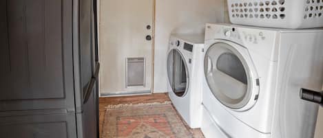 A laundry room with two front-loading washing machines, a drying rack, and a door.