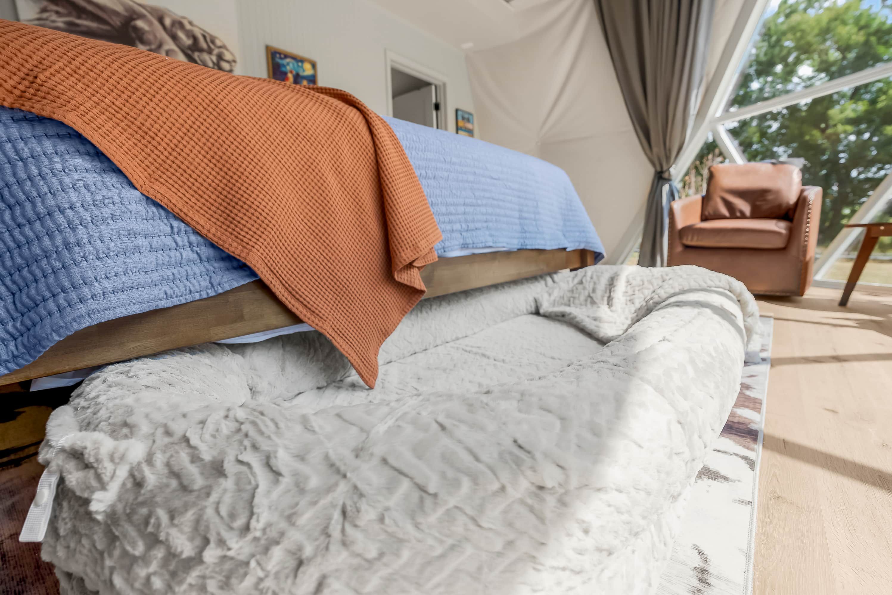 Una cama con un edredón azul, una manta naranja y una manta blanca con textura.