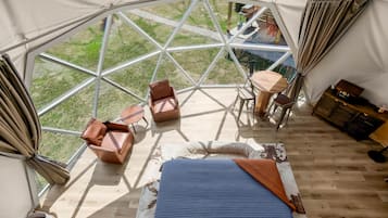 Una carpa con techo de cristal geométrico, amueblada con sillones de cuero, una mesita y una cama con cubrecama azul.