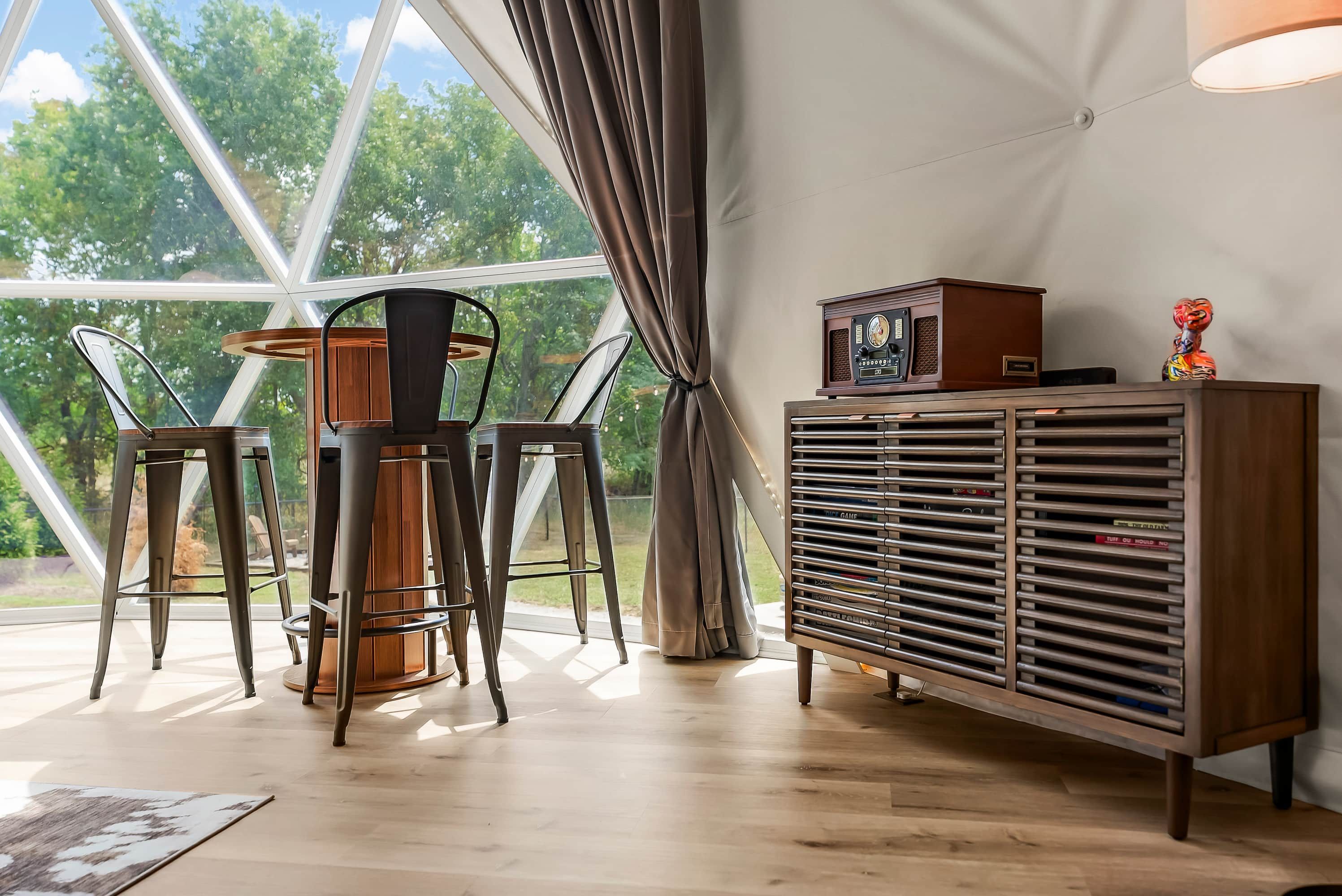 Une pièce avec une grande fenêtre, une table avec des chaises et un meuble contenant une radio.