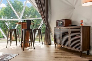 A room with a large window, a table with chairs, and a cabinet with a radio.