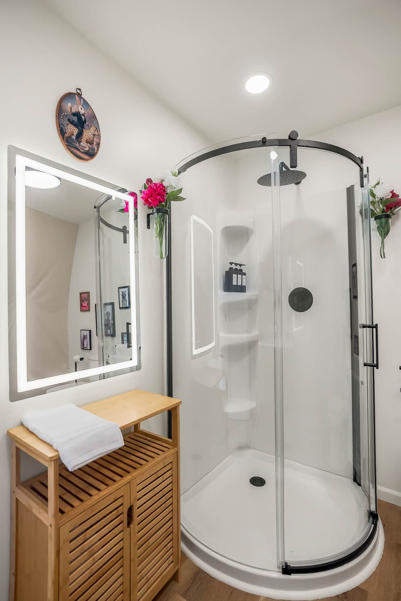 A modern bathroom with a glass-enclosed shower, a wooden vanity, and a mirror with a decorative frame.