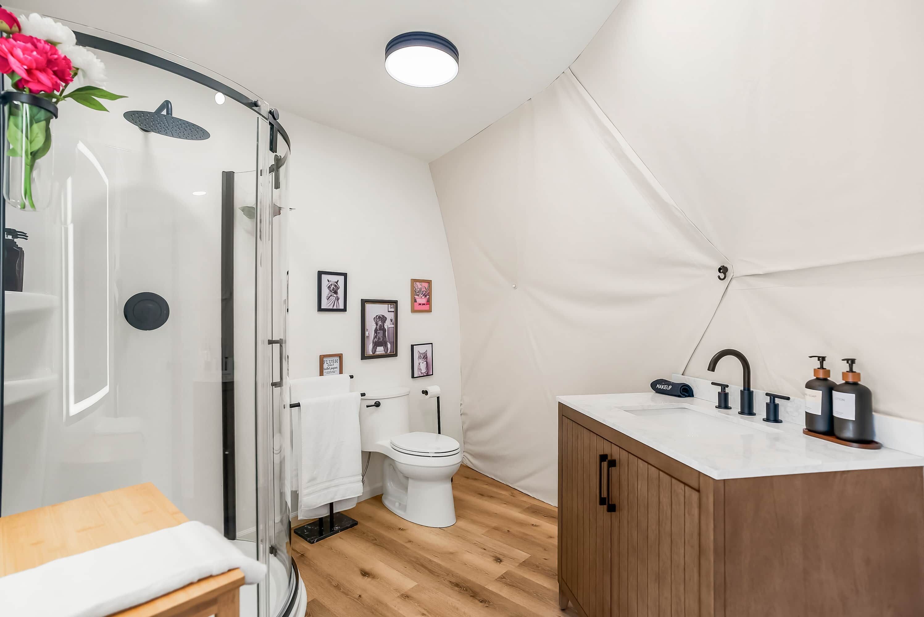 Une salle de bain moderne avec une douche à parois de verre, des toilettes blanches, un meuble en bois et un lavabo blanc avec des robinets noirs.