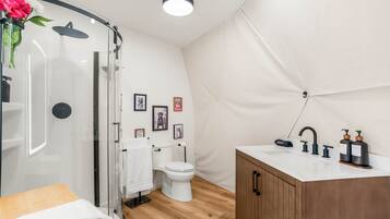 Une salle de bain moderne avec une douche à parois de verre, des toilettes blanches, un meuble en bois et un lavabo blanc avec des robinets noirs.