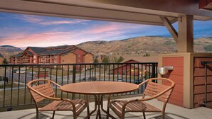 Uma varanda com mesa e cadeiras, vista para uma área residencial com edifícios e montanhas.