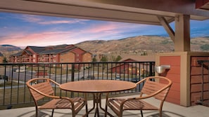 Un balcon avec une table et des chaises, donnant sur un quartier résidentiel avec des immeubles et des montagnes.
