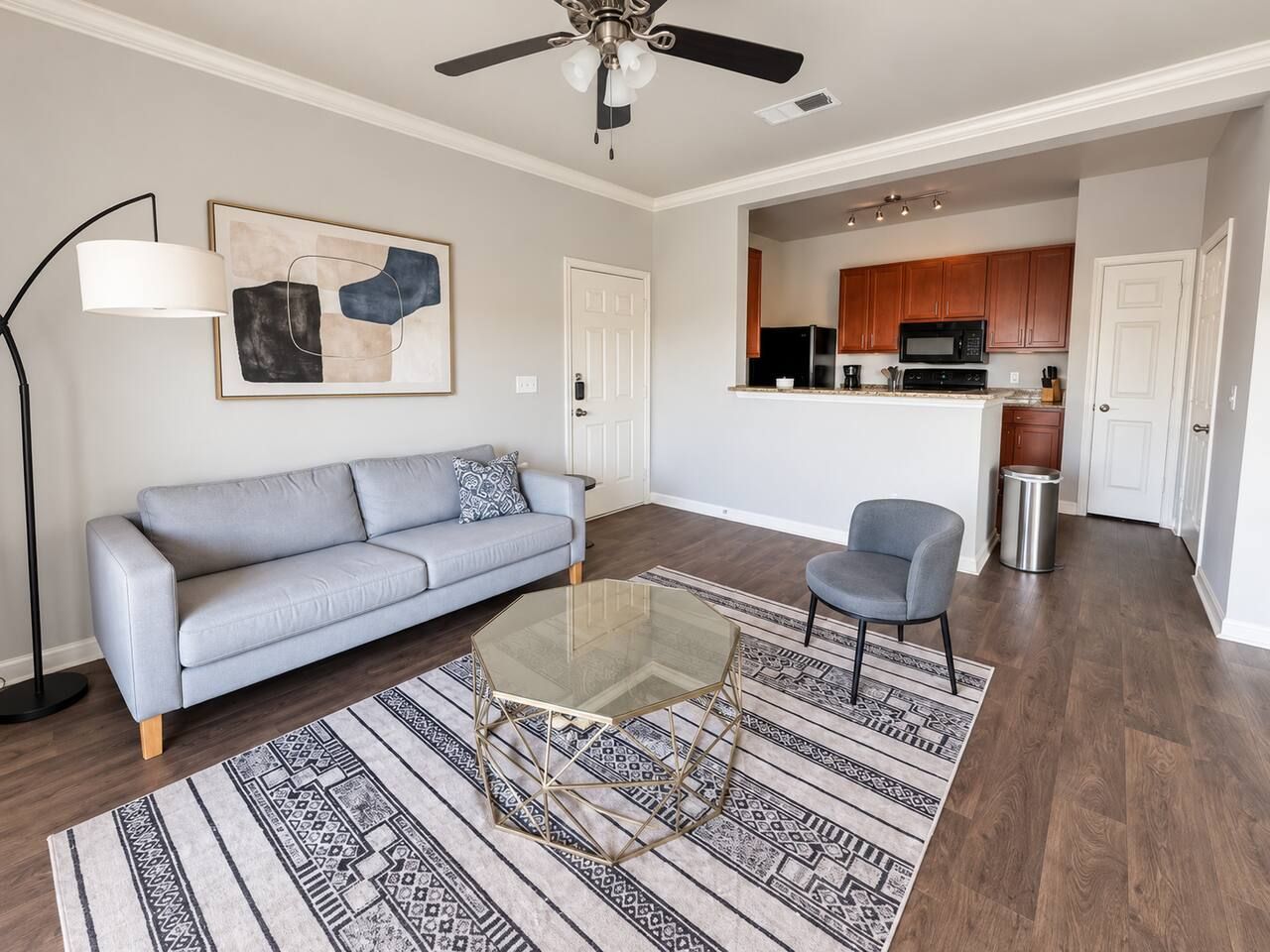 Un salon comprenant un canapé, une table basse en verre, un tapis à motifs, une lampe sur pied et un ventilateur de plafond.