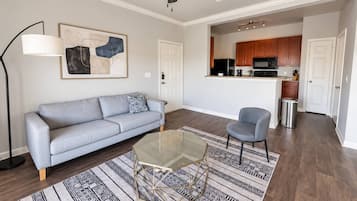 Un salon comprenant un canapé, une table basse en verre, un tapis à motifs, une lampe sur pied et un ventilateur de plafond.