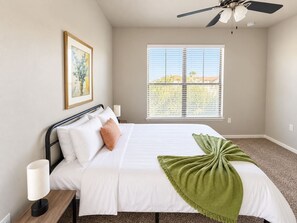 A bedroom with a bed, bedside lamps, a ceiling fan, a window with blinds, and a framed picture on the wall. - Sleepover | Serene 1BD/1BA + Gym - Corpus Christi (Corpus Christi)