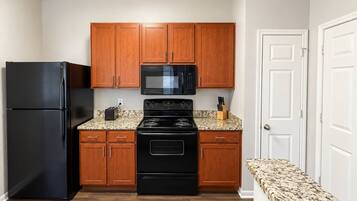 A compact kitchen with wooden cabinets, a black refrigerator, a microwave, and a stove.