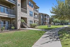 A multi-story residential building with balconies, a stone facade, and a well-maintained lawn. - Sleepover | Serene 1BD/1BA + Gym - Corpus Christi (Corpus Christi)