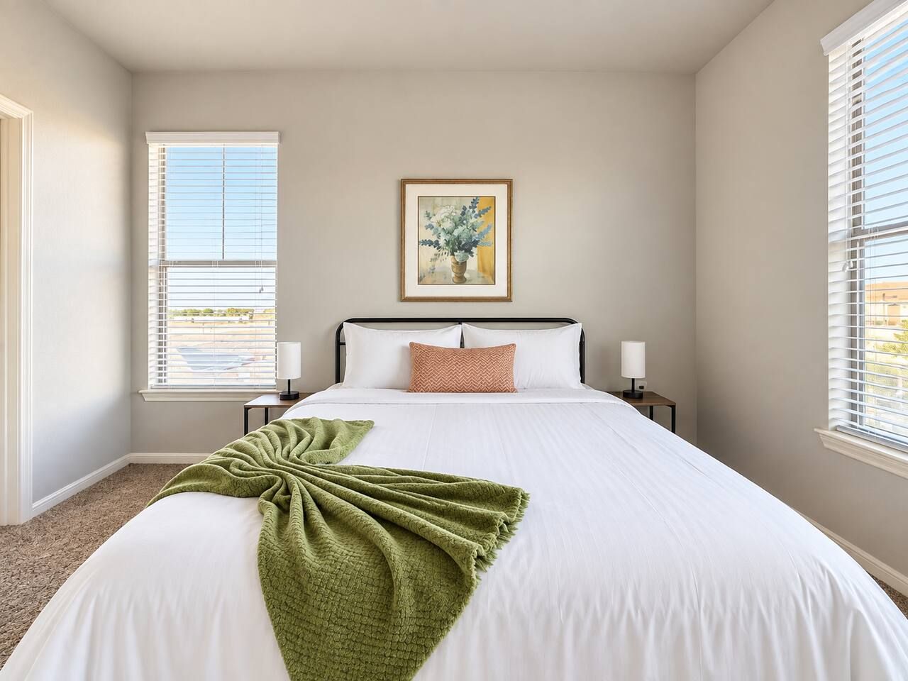 A bedroom with a large bed, a framed picture on the wall, and a window with blinds.