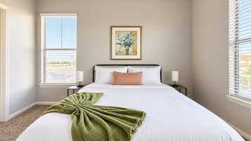 A bedroom with a large bed, a framed picture on the wall, and a window with blinds.