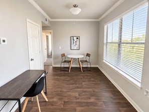 A room with a dining table and chairs, a ceiling light, a window with blinds, and a door. - Sleepover | Serene 1BD/1BA + Gym - Corpus Christi (Corpus Christi)