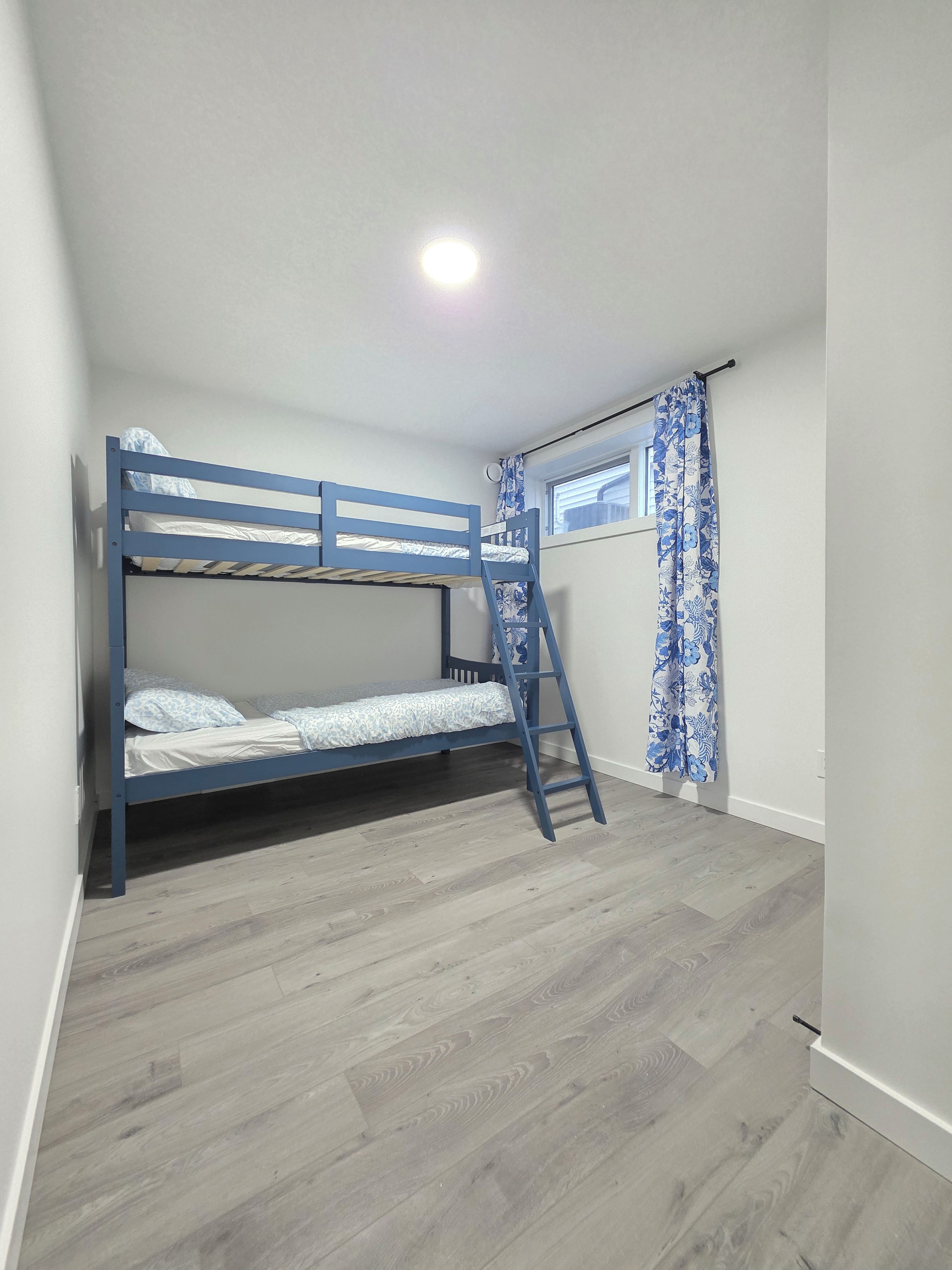 Ein Zimmer mit Etagenbett, einem Vorhangfenster und Holzboden.