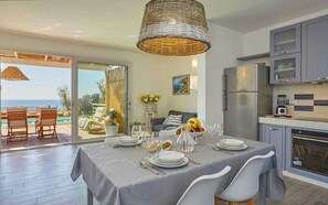 Un comedor con una mesa preparada para cuatro, una cocina con electrodomésticos modernos y vista al océano a través de un ventanal.