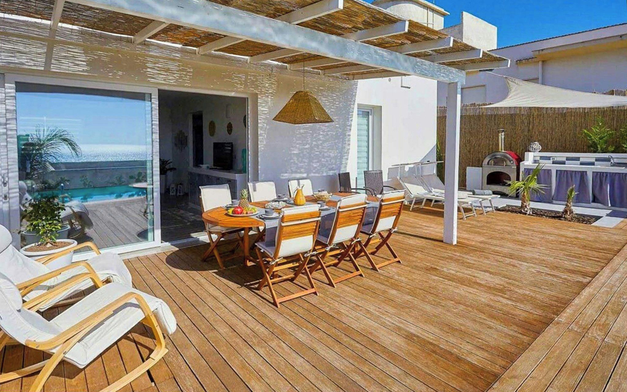 A wooden deck with a dining table and chairs, a grill, and a poolside area.