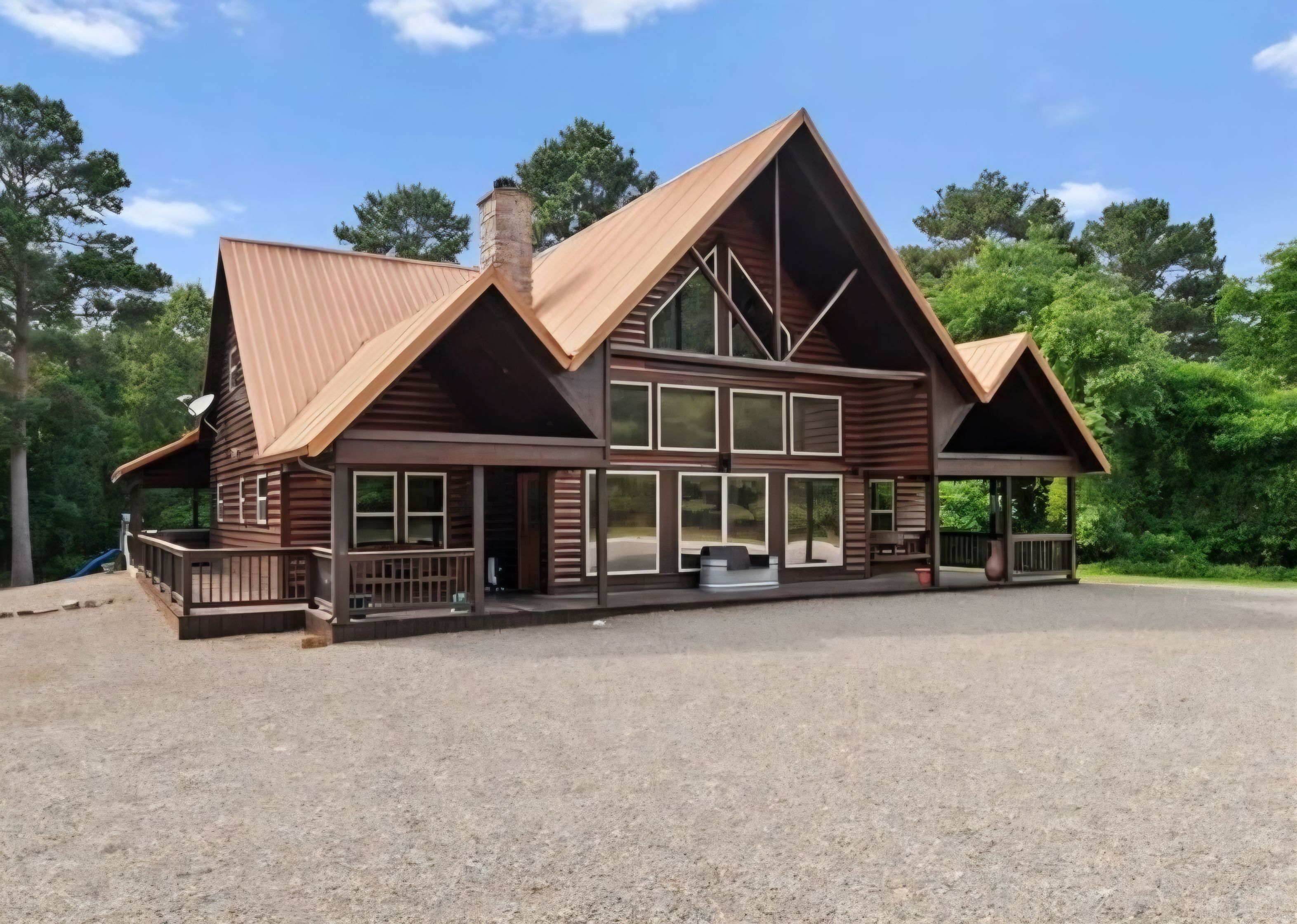 Une grande maison de style rustique, construite en bois, avec un toit à pignon bien visible, de nombreuses fenêtres et une véranda couverte.