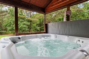 A hot tub with a wooden roof and a view of a forested area. - S'mores at Sunset-Luxury 3-bedroom cabin located in the heart of Broken Bow. (Broken Bow)