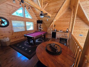 A wooden interior with a pool table, a billiards table, a round table with a centerpiece, and a ceiling fan. - S'mores at Sunset-Luxury 3-bedroom cabin located in the heart of Broken Bow. (Broken Bow)