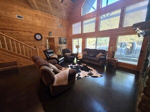 A log cabin interior with a staircase, leather sofas, a cowhide rug, and large windows. - S'mores at Sunset-Luxury 3-bedroom cabin located in the heart of Broken Bow. (Broken Bow)