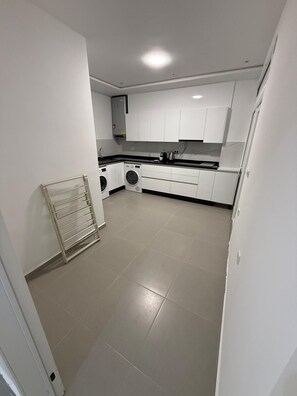 A compact kitchen with white cabinets, a washing machine, and a built-in oven. - Palm House Tanger Apartment 02 (Tanger)