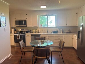 A kitchen with white cabinets, a microwave, a stove, a sink, and a refrigerator. There is a round glass table with four chairs. - Spacious Home - 10 minutes to Downtown (Nashville)