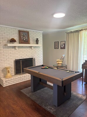 A billiards table in a room with a brick fireplace, a framed picture above it, and a billiard cue on the table. - Spacious Home - 10 minutes to Downtown (Nashville)