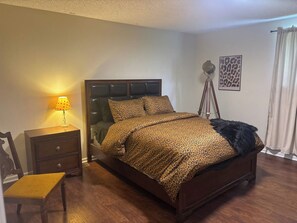 A bedroom with a bed, a nightstand, a chair, a lamp, a floor lamp, and a wall with a framed picture. - Spacious Home - 10 minutes to Downtown (Nashville)