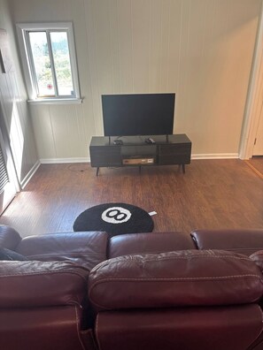 Ein Wohnzimmer mit einem Ledersofa, einer schwarzen Unterhaltungsanlage und einem Fenster mit Blick auf Grünflächen.