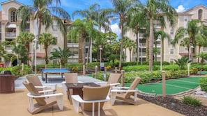 Un patio con mobiliario exterior, palmeras y una cancha de tenis.