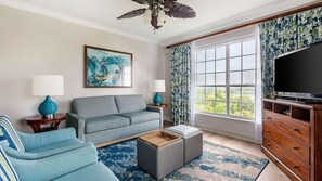 Una sala de estar con sofá, reposapiés y televisor sobre un mueble de madera.