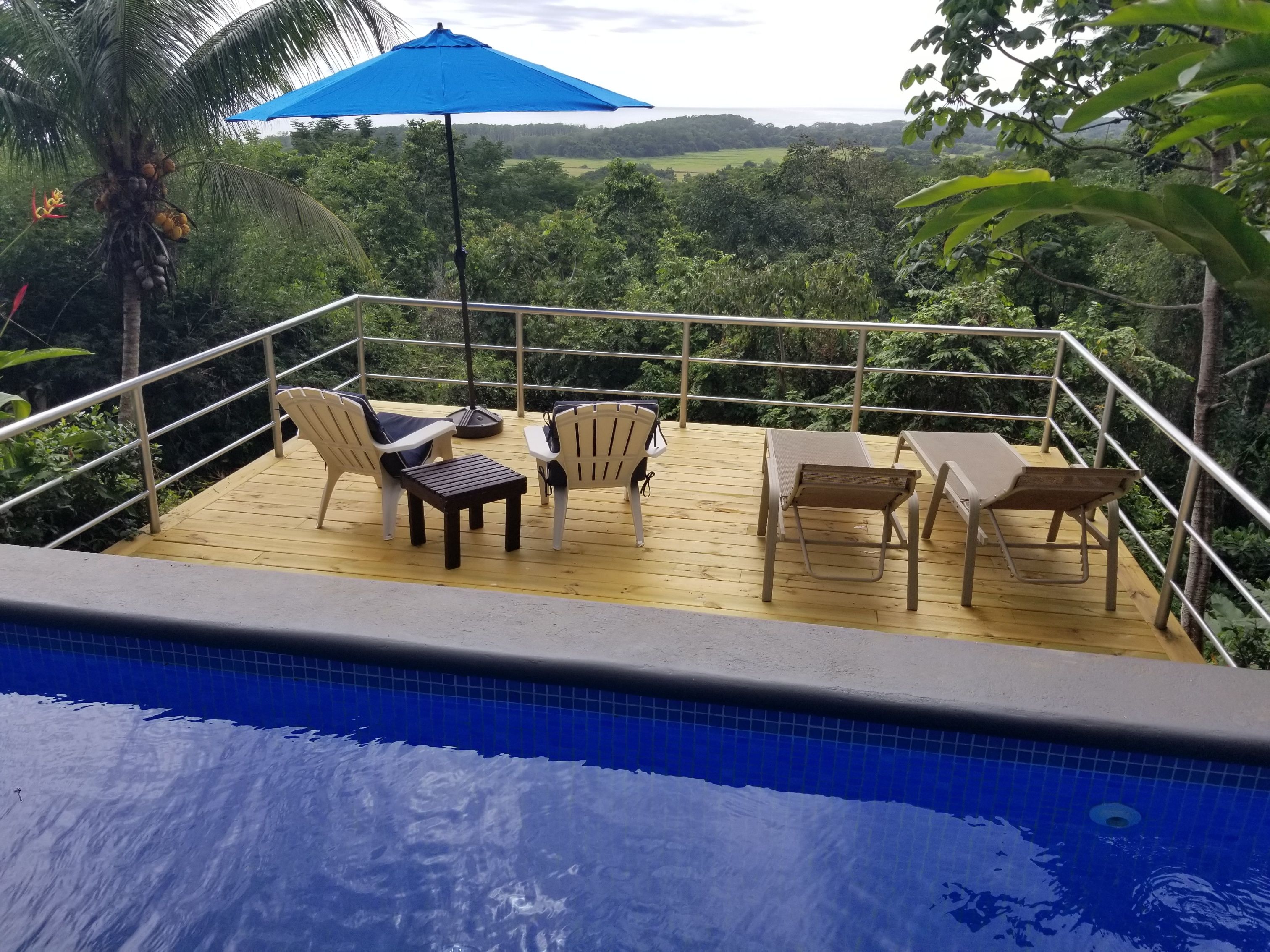 A wooden deck with outdoor seating, overlooking a pool and lush greenery.