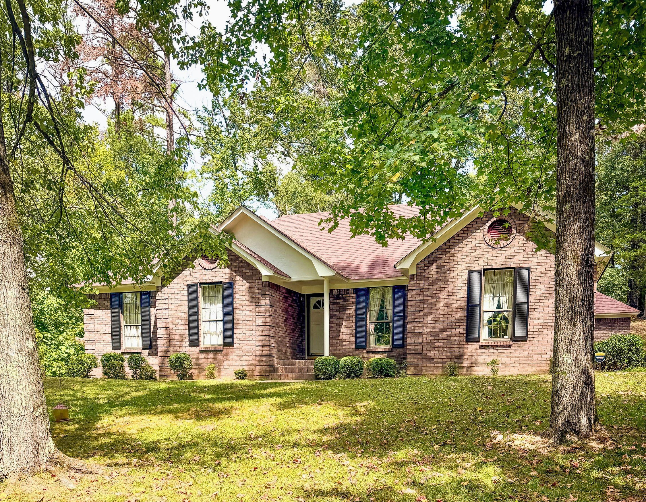 A two-story brick house with a red roof, surrounded by trees and a well-maintained lawn.