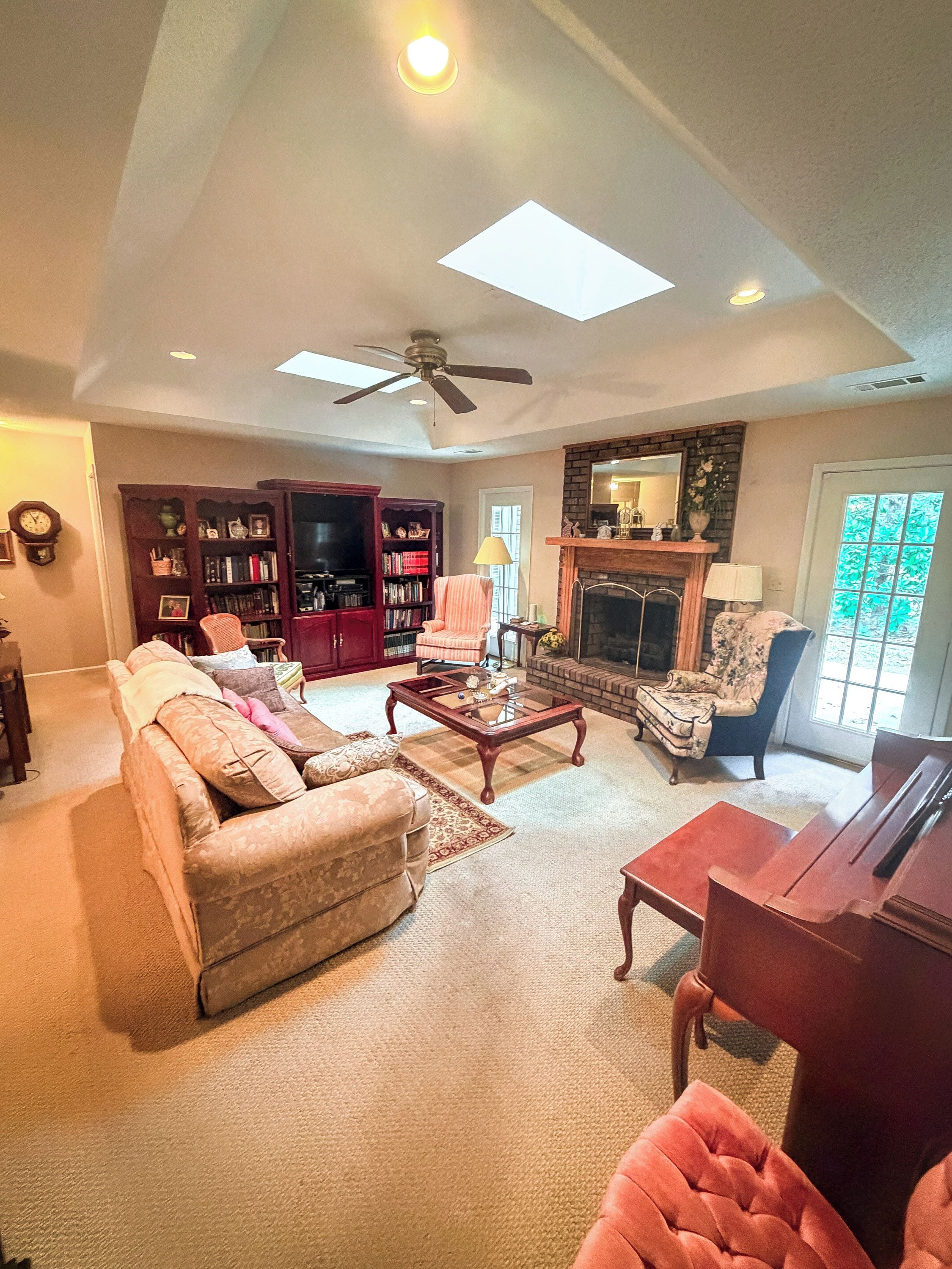 A spacious living room with a fireplace, a ceiling fan, and a large bookshelf.