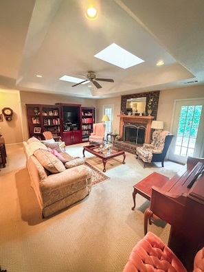 A spacious living room with a fireplace, a ceiling fan, and a large bookshelf. - Home in Golf Course Community- minutes from everything (Oxford)