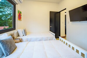 Ein Schlafzimmer mit zwei Betten, einem Fenster mit Blick auf Bäume und einem an der Wand befestigten Fernseher.