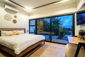 Ein Schlafzimmer mit Bett, Nachttisch, Fenster mit Blick auf Bäume und Deckenventilator.