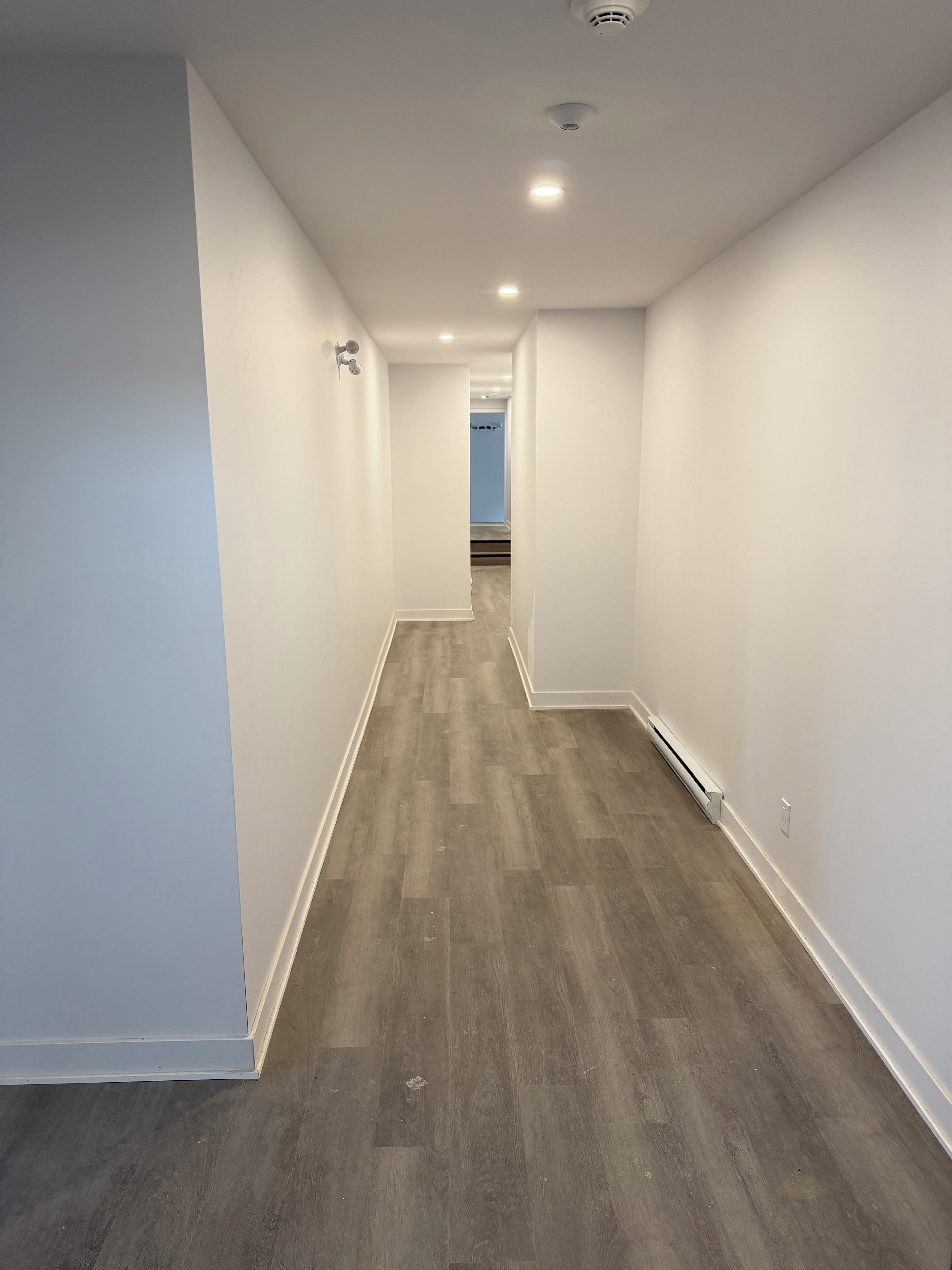 Un pasillo con paredes blancas y piso de madera que conduce a una habitación con una pared azul.