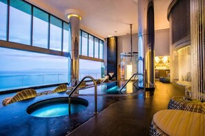 A luxurious indoor pool area with clear views of the ocean, a seating area with loungers, and a bar with a decorative column. - Garza Blanca Preserve Puerto Vallarta- Everything you love at one place (Puerto Vallarta)