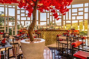 A restaurant with a bar area, tables, chairs, and a large potted tree. - Garza Blanca Preserve Puerto Vallarta- Everything you love at one place (Puerto Vallarta)
