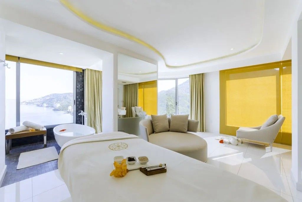 Een moderne hotelkamer met een groot bed, een zithoek met een bank, een badkuip en uitzicht op de omgeving.