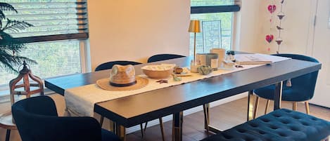 A dining area with a long table, chairs, and benches. There are hanging lights, a mirror, and a wall decoration.