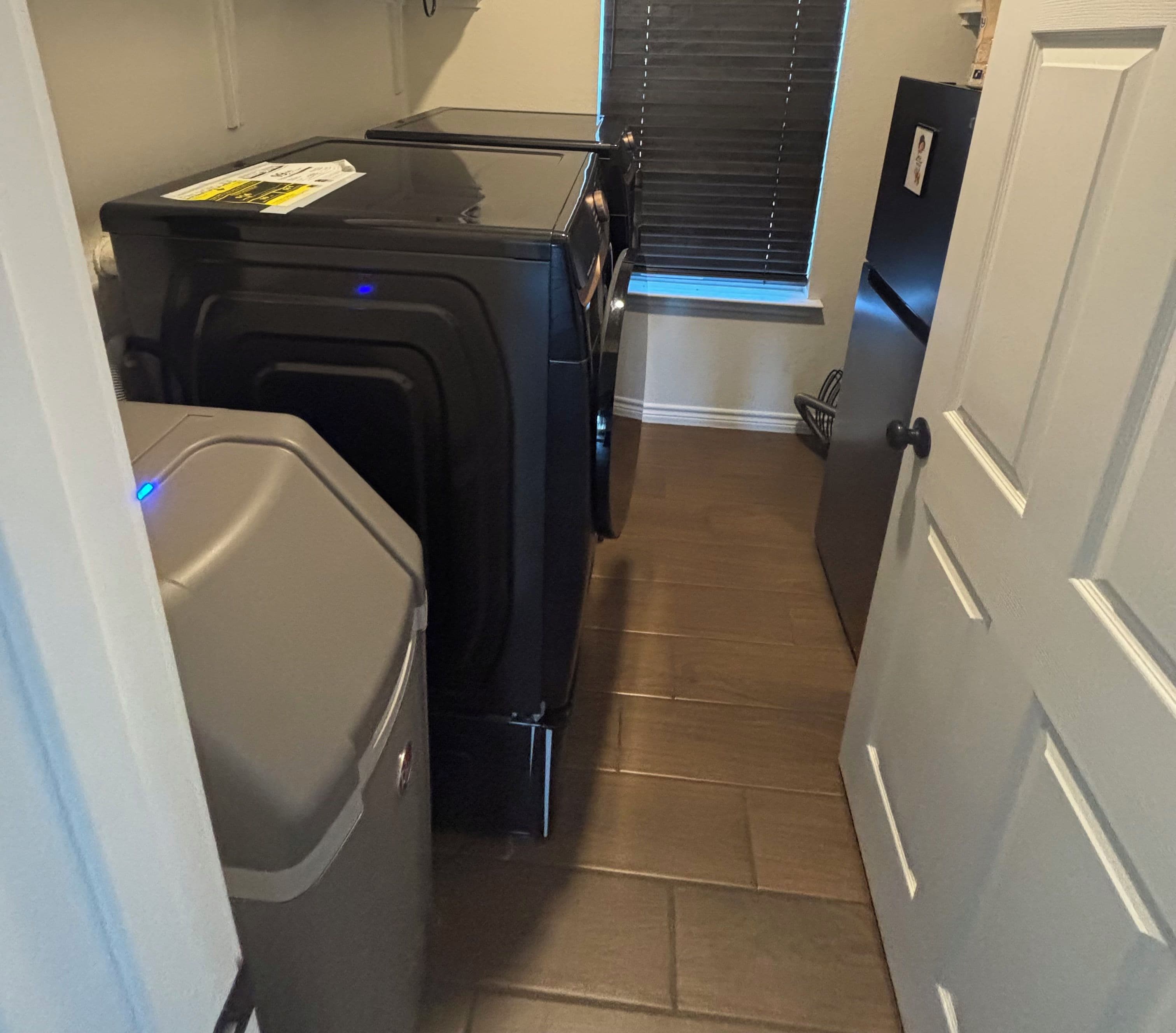 A compact room with a compact washer and dryer, a small trash bin, and a door leading to a staircase.