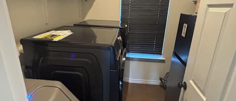 A compact room with a compact washer and dryer, a small trash bin, and a door leading to a staircase.
