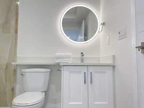 Un baño moderno con inodoro, lavabo con espejo y un armario.