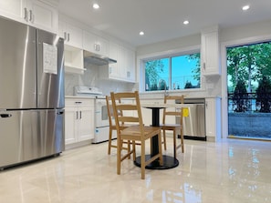 Una cocina moderna con armarios blancos, electrodomésticos de acero inoxidable y un comedor con sillas de madera.