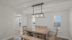 Uma área de refeições com mesa de madeira e bancos, luminária pendente e vista pela janela com persianas.