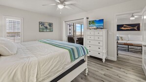 Quarto com cama, cômoda, televisão e vista para a praia.