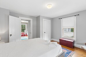Ein Schlafzimmer mit einem großen Bett, einem Fenster mit Jalousien, einer roten Kommode und Blick ins Freie.